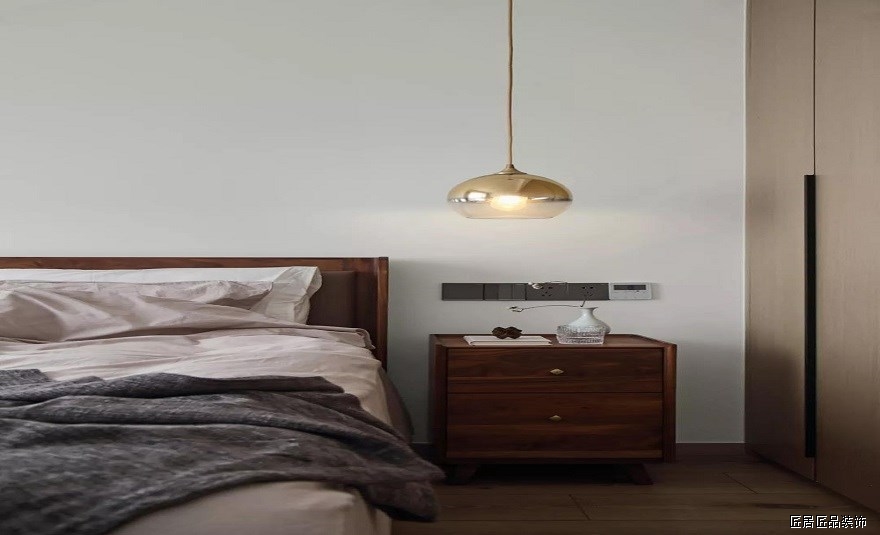 主卧室的設計非常的素雅，木質和布藝靠背的床、複古的床頭櫃，淺色調的背景牆，還有一(yī)盞銅質吊燈，呈現出安靜優雅的氛圍。